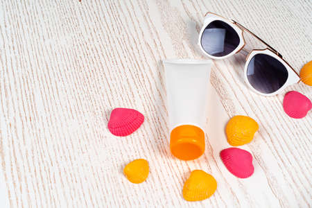 Sunblock lotion with colored seashells on wooden board