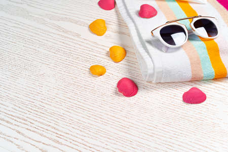 Colorful striped towel with sunglasses and seashells on wooden board