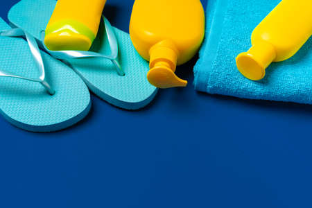 Suntan products in yellow bottles with beach towel and flip-flops