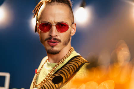 Young fashionable man in pink sunglasses playing guitar with joyの写真素材