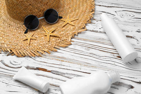 Straw hat, sunglasses and sunscreen bottle on wooden background
