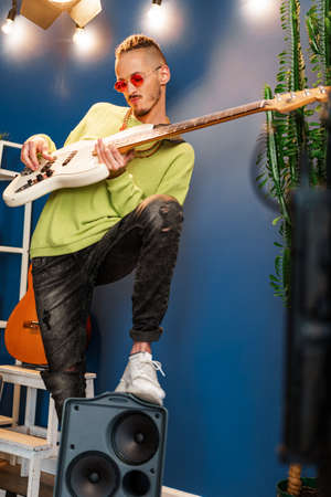 Young fashionable man in pink sunglasses playing guitar with joy
