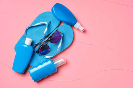 Blue flip-flops with sunscreen and sunglasses on pink background