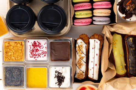 Assortment of desserts in boxes on white wooden background