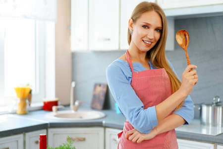 Attractive young woman in red apron standing in her kitchenの写真素材