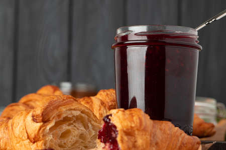 Fresh croissants with berry jam on dark wooden board