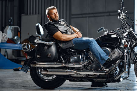 Bearded motorcyclist in black leather clothing with his motorbike