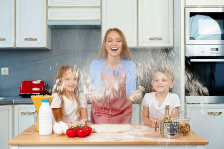 Young blonde woman, mother and her kids having fun while cooking doughの写真素材