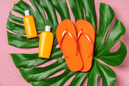 Orange flip-flops with sunscreen creams on big monstera leaf on pink backgroundの写真素材
