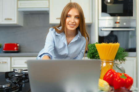 Young blonde woman with long hair using laptop in a kitchen