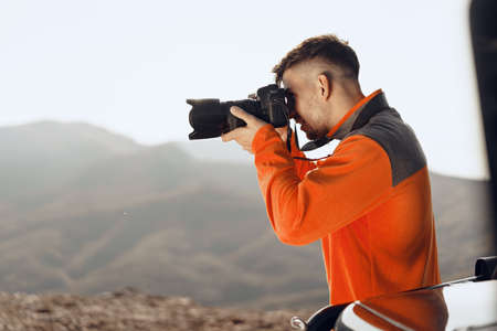 Young man traveler taking photos of mountains with professional camera