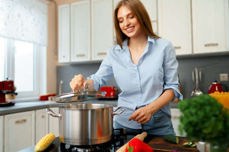 Nice young woman cooking something by the stove in her kitchenの写真素材
