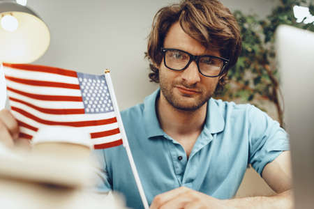 Young bearded businessman sitting at table with laptop and american flagの写真素材