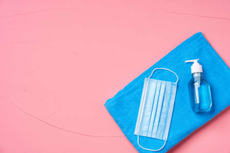 Blue towel with protective mask and hand sanitizer on pink background