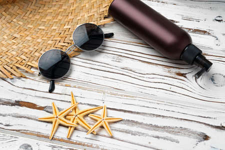 Straw hat, sunglasses and sunscreen bottle on wooden background