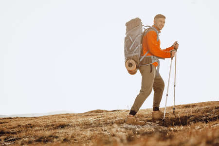 Man traveler with trekking sticks going up the mountain