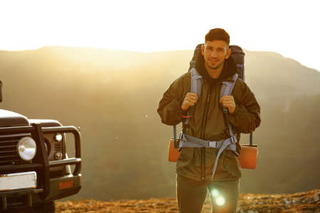 Portrait of a young traveler man in hiking equipment standing near his off-road car