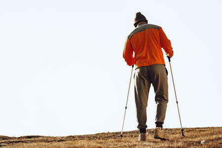Man traveler with trekking sticks going up the mountain