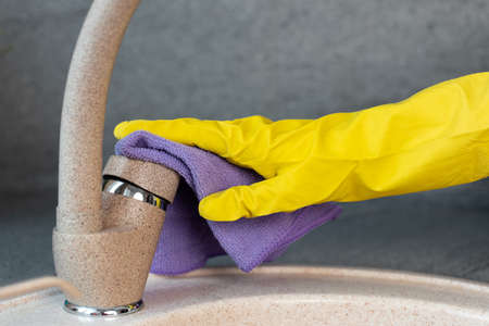 Hands in yellow gloves cleaning a sink with a sponge