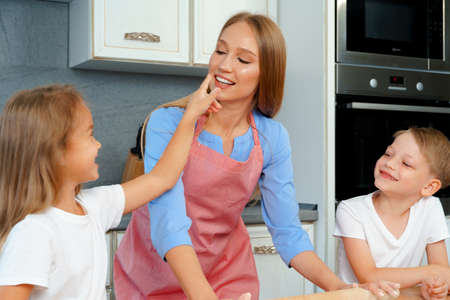 Young blonde woman, mother and her kids having fun while cooking doughの写真素材