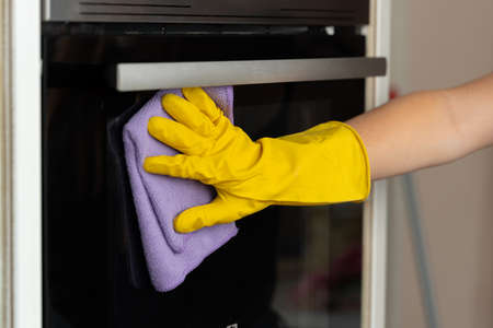 Womans hand in yellow glove cleaning door of an oven