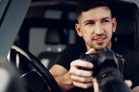 Attractive man photographer taking a photo while sitting in his carの写真素材