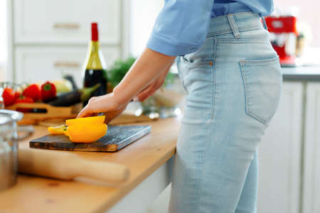 Young blonde caucasian woman cutting vegetables for salad at her kitchenの写真素材