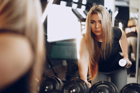 Back view of a woman training her hands with a dumbbell in a gymの写真素材