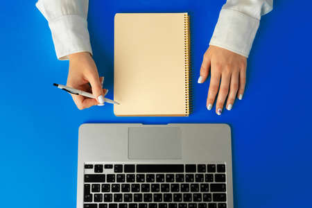 Female hand writing in a notebook on table with laptop, view from aboveの写真素材
