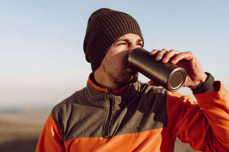 Young man traveler drinking from his thermocup while halt on a hikeの写真素材
