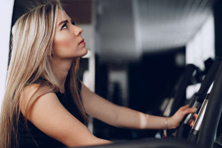 Attractive young blonde woman exercising on cardio training apparatus