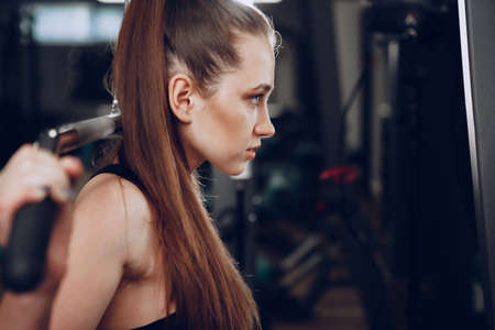 Attractive young woman doing exercises for the muscles of the arms and back in a gym