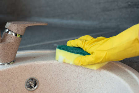 Hands in yellow gloves cleaning a sink with a sponge