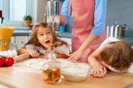 Young blonde woman, mother and her kids having fun while cooking doughの写真素材