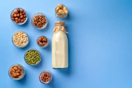 Vegetable milk concept with milk bottle and bowls with grains on blue background top view