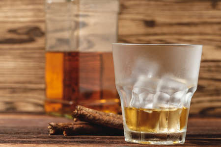 Glass of whiskey and rolled cigars on wooden table