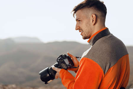 Young man traveler taking photos of mountains with professional cameraの写真素材