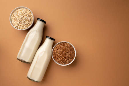 Two glass bottles of non-dairy vegan milk with bowls of grains top viewの写真素材