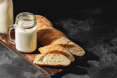 Glass of milk with sliced baguette on wooden board