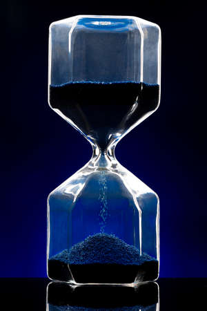 Hourglass illuminated on dark blue background close up