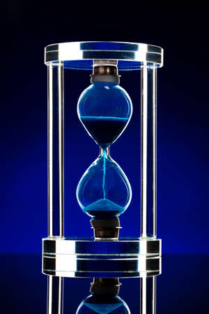 Hourglass illuminated on dark blue background close upの写真素材