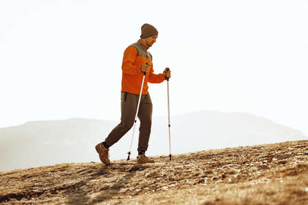Man traveler with trekking sticks going up the mountain