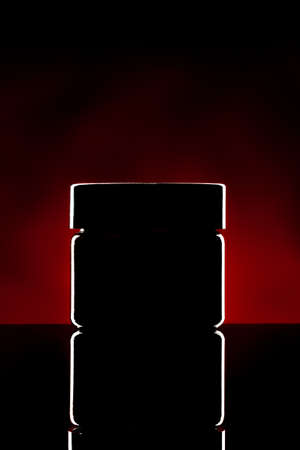 Plastic jar with cosmetics illuminated on dark backgroundの写真素材