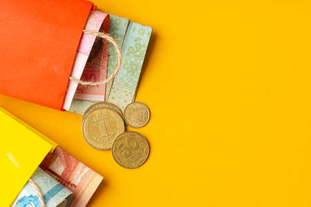 Small red shopping bag with ukrainian currency hryvnia on yellow background