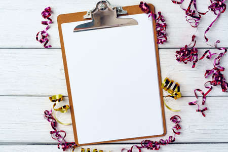 Clipboard with blank sheet of paper and party streamers on white wooden tableの写真素材