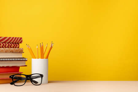 Cup of pencils and notepads on desk against yellow backgroundの写真素材