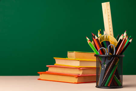 School supplies on wooden desk against green chalkboardの写真素材