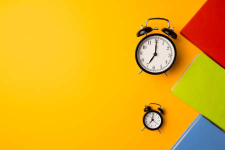 Three color hardcover notepads and alarm clock on yellow backgroundの写真素材