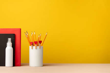 Cup of pencils and notepads on desk against yellow backgroundの写真素材