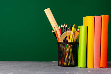 School supplies on wooden desk against green chalkboard